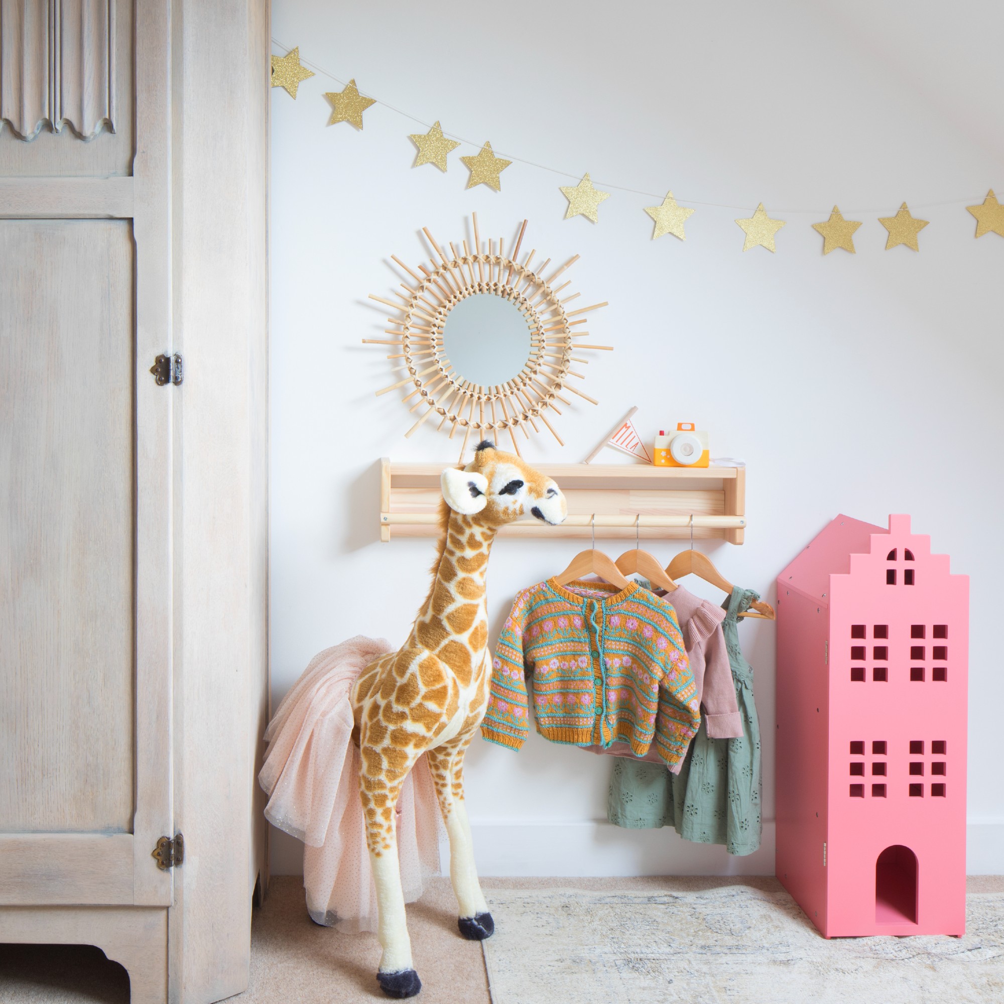 A nursery with a shelf displaying kids' clothes and a star bunting decorating the wall