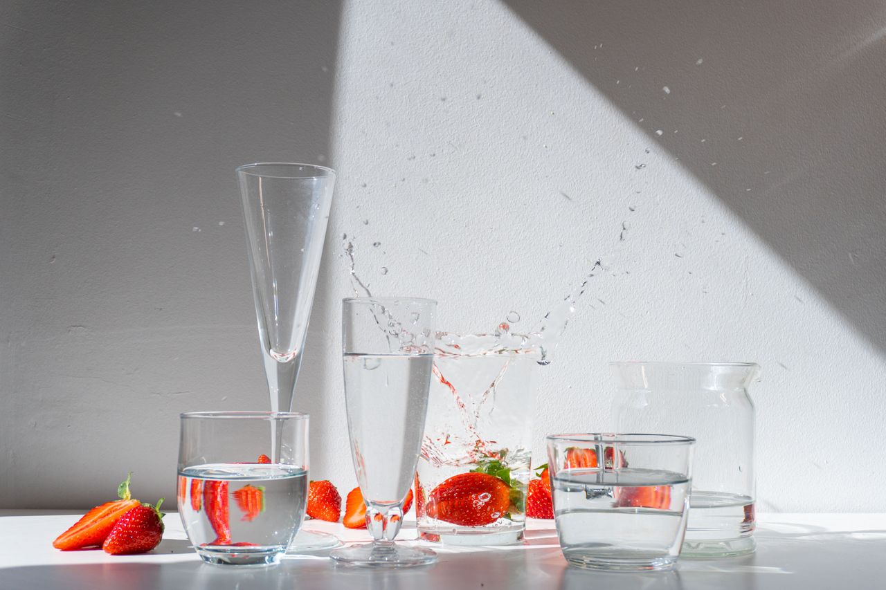 A dynamic display of glasses filled with water, fresh strawberries, and splashes, illuminated by dramatic light against a wall