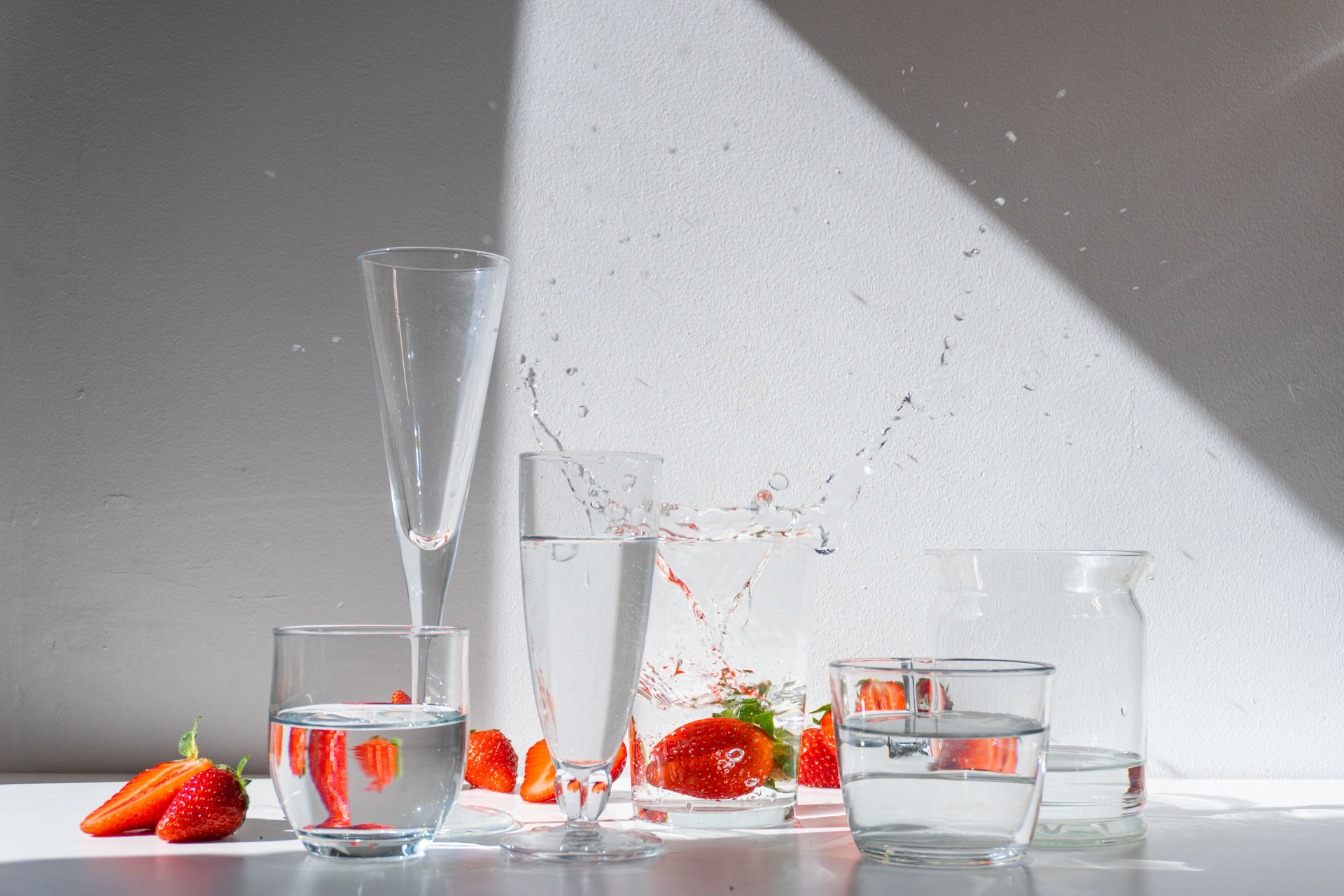 A dynamic display of glasses filled with water, fresh strawberries, and splashes, illuminated by dramatic light against a wall