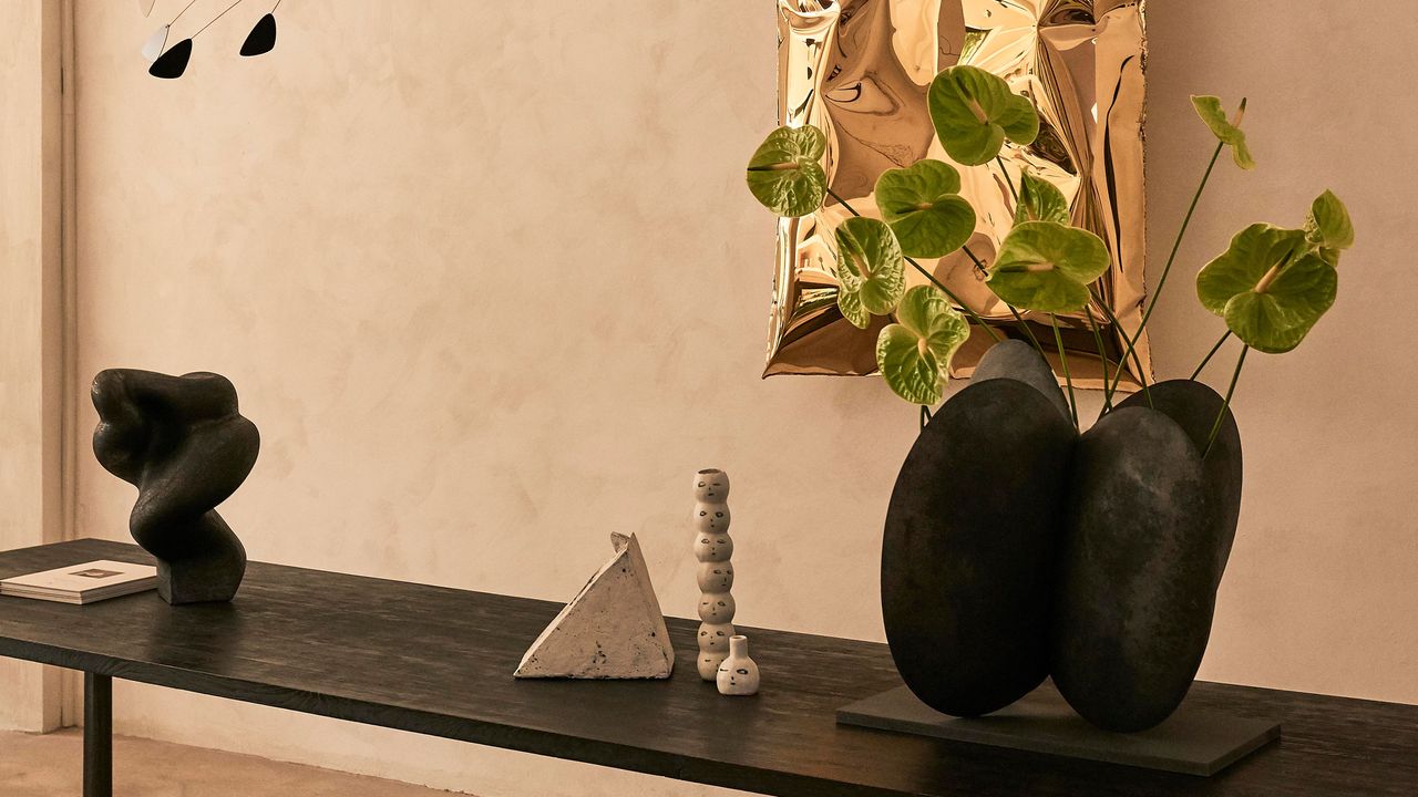 green anthurium in a black sculptural vase n a limewash backdrop with a gold artwork on the wall