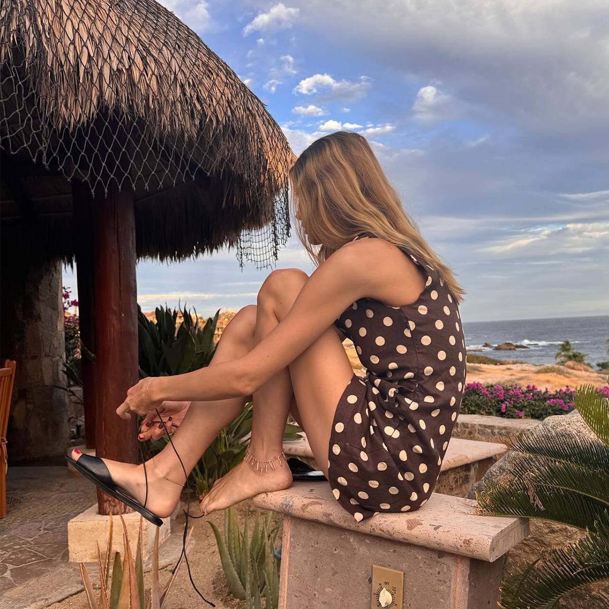 Courtney Grow wearing a brown polka dot Posse dress with lace-up sandals.