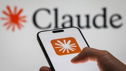 Anthropic Claude logo and branding pictured on a smartphone screen held in hand, with separate branding pictured in background.