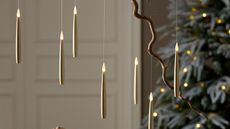 A set of six white LED taper candles hanging from fishing line from a branch. A christmas tree is out of focus in the background