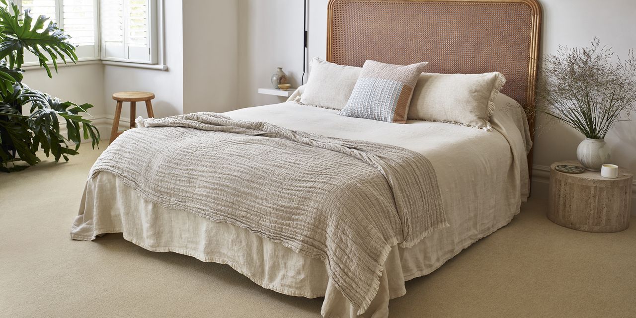 a neutral bedroom with a large bed in the centre and beige carpet on the floor