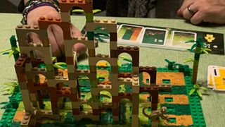 The arches of Lego Monkey Palace, with clasped hands behind it leaning on a green surface beside cards