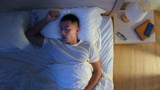 Bedtime routines for adults: A man asleep in bed with one arm above his head