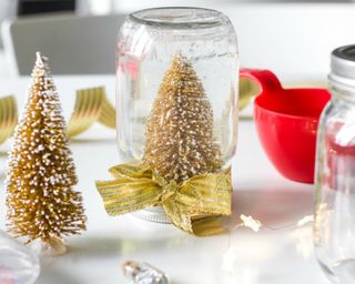 A mason jar Christmas snow globe with gold miniature tree decor