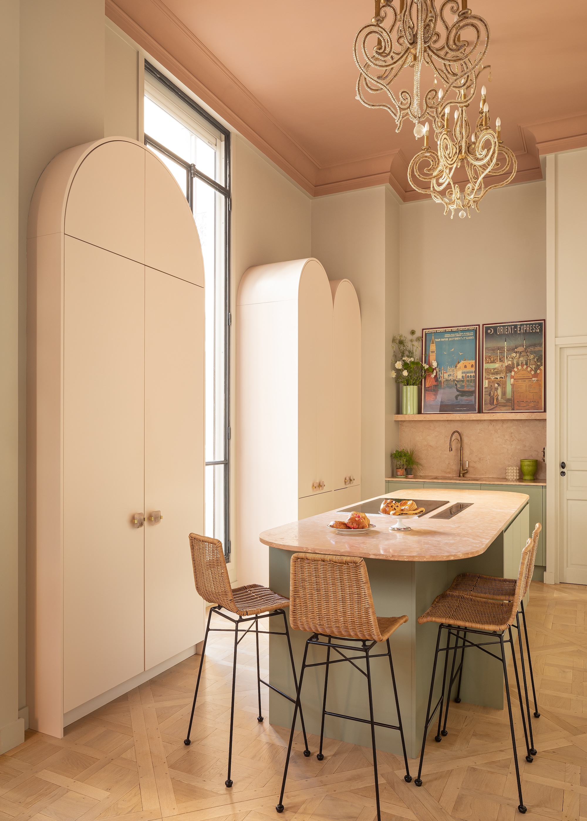 a curved kitchen island with bar stools and curved long length cabinets next to it. Above the island are large lights.