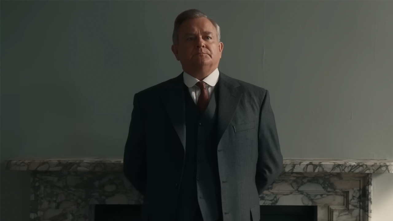 Hugh Bonneville in a gray suit, standing in front of a fire place, in Downton Abbey: The Grand Finale