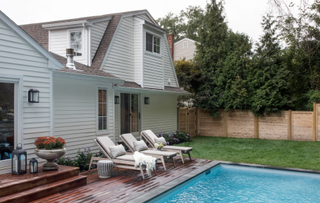 Pool surrounded by grass, dark-colored decking and three sun loungers