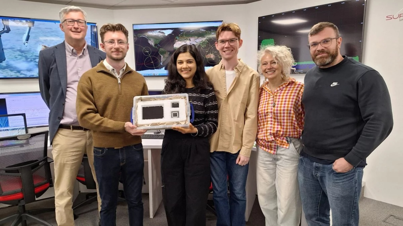 A group of researchers holding up a satellite in a control room