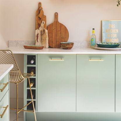 green kitchen cabinets with gold bar stool and breadboards on worktop