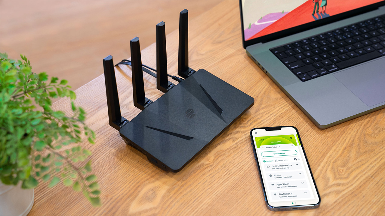 ExpressVPN Aircove router on a brown table, next to smartphone and laptop with the ExpressVPN app open