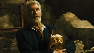 Pierce Brosnan holds his Dr Fate helmet while looking up stoically in Black Adam.