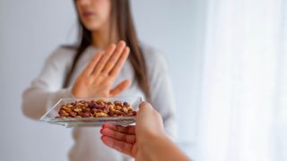 A woman holding up her hand and saying no to a bowl of nuts because of allergies