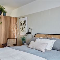 how to decorate a guest bedroom, neutral bedroom with wood paneling on one side and tongue and groove on the other, rattan bed, artwork, plants 