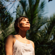 Woman with closed eyes and sunshine on her face with palm trees behind her - she looks like she could have used one of the best fake tans