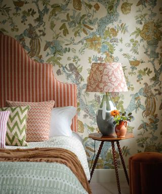 Floral wallpaper in cream and white with stripey headboard and coral lamp