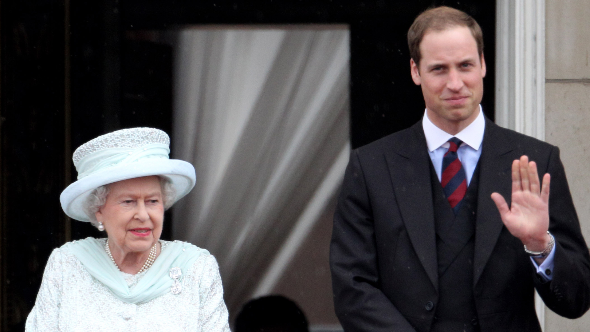 Queen Elizabeth II wears a blue jacket and matching hat and Prince William wears a suit