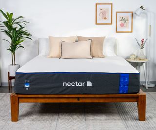 A Nectar mattress on a bed with pillows against a white bedroom wall.