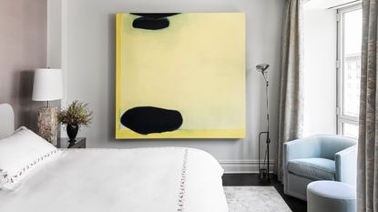 modern bedroom with large yellow artwork on the wall, gray wall, pink wall, white bedding, with light blue armchair with ottoman under a window next to a floor lamp