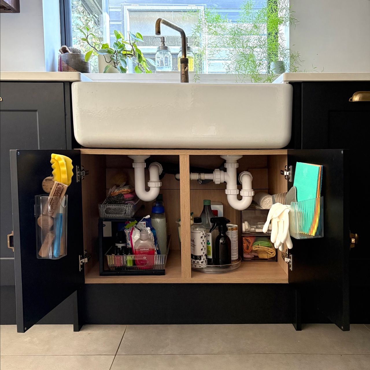 Cupboard under a belfast sink with doors open showing various storage solutions including pull-out rack, lazy susan and stacked drawers to store cleaning products