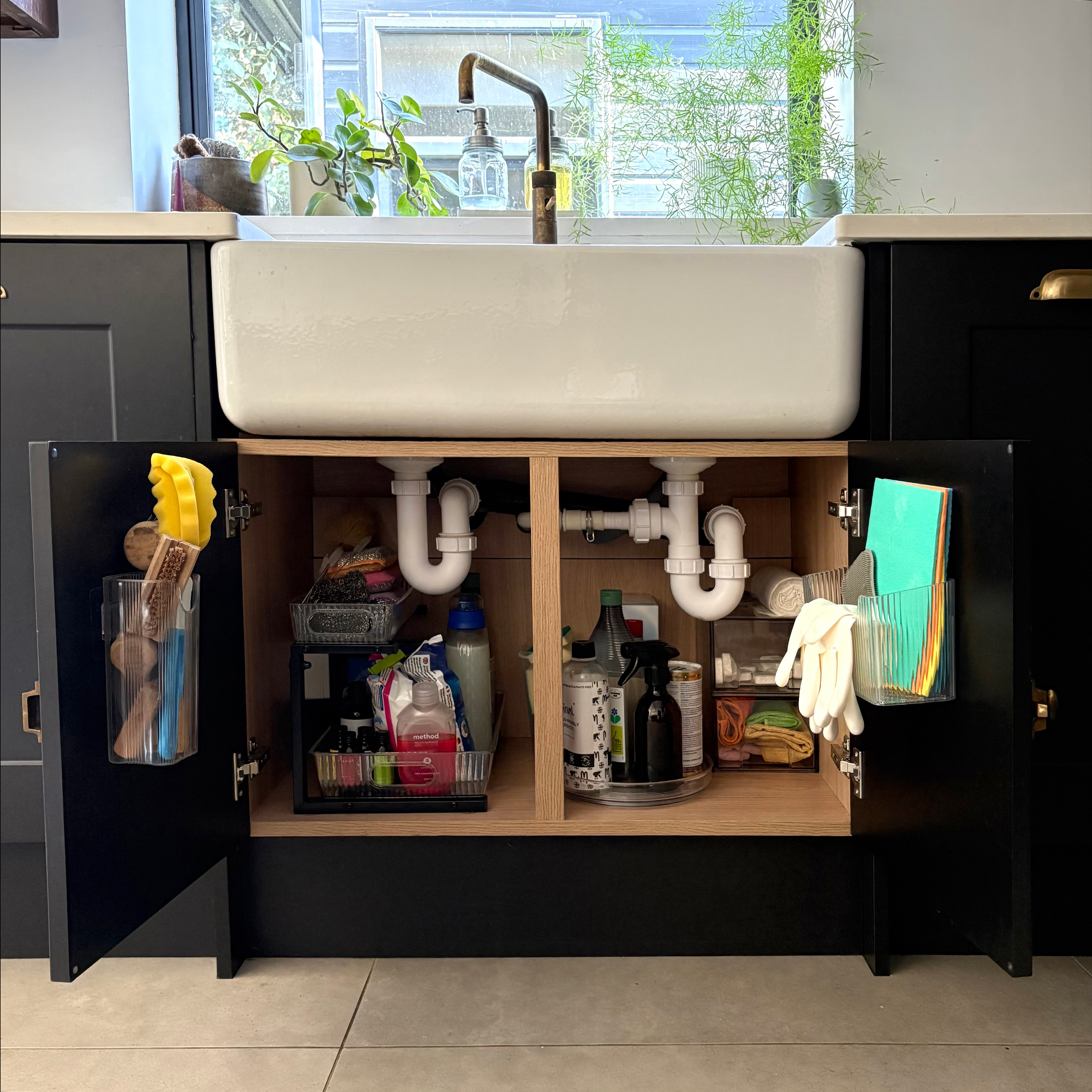 Cupboard under a belfast sink with doors open showing various storage solutions including pull-out rack, lazy susan and stacked drawers to store cleaning products
