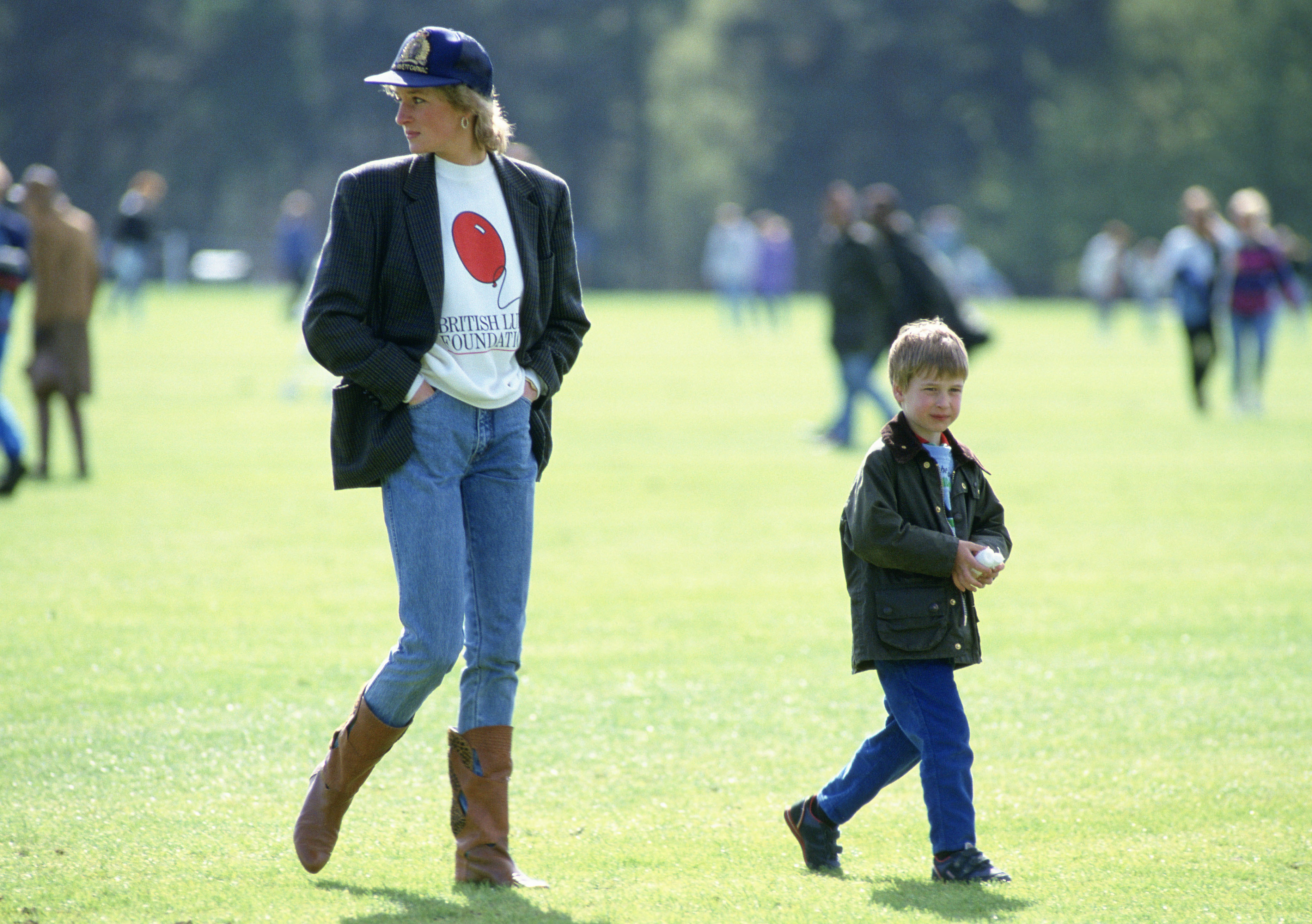 Princess Diana wearing jeans and a blazer walking across a field with Prince William