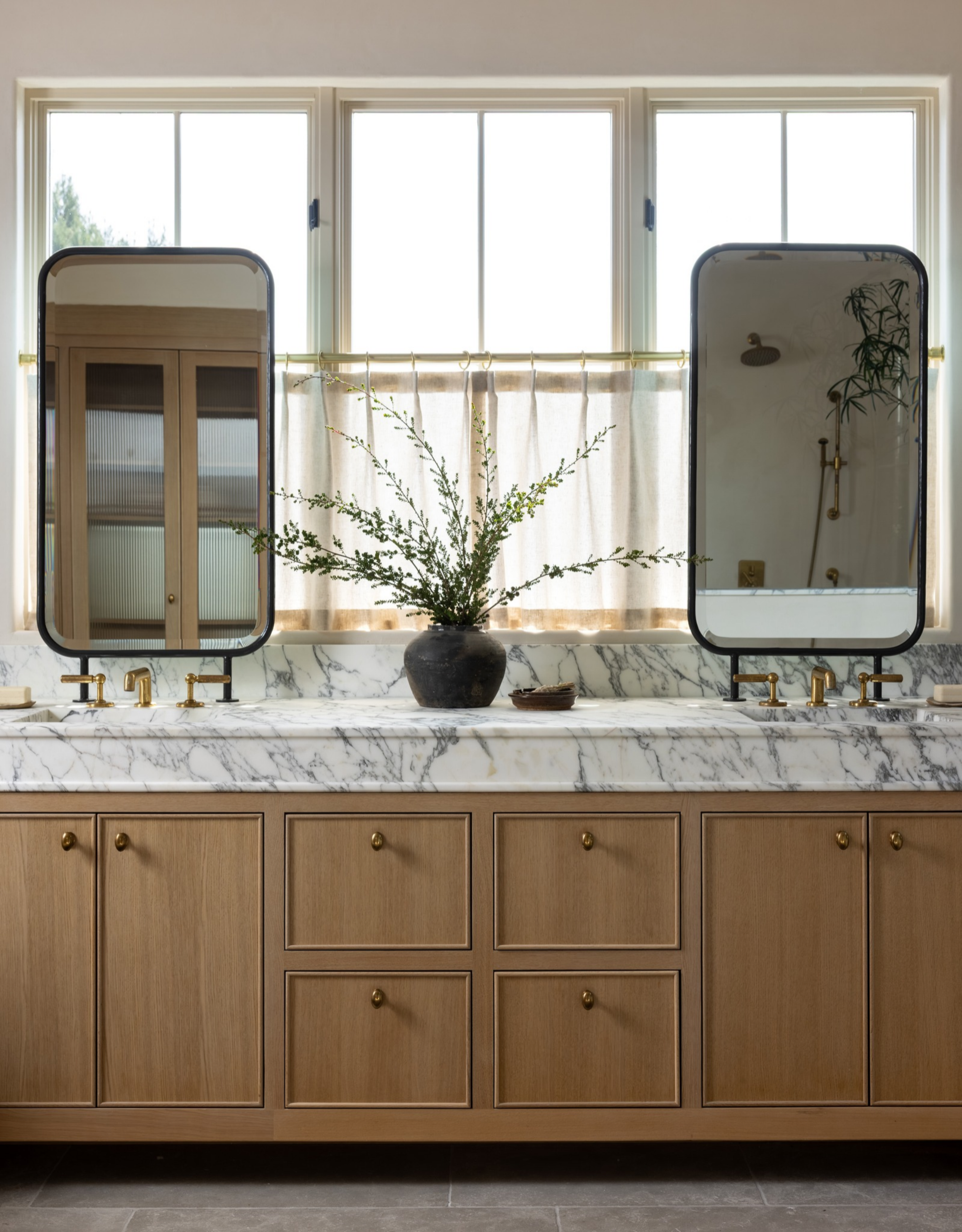 his and hers sink in marble with wooden cabinetry below and two mirrors in front of a window