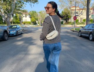 Woman in a striped T-shirt and jeans carrying a cream crossbody bag.