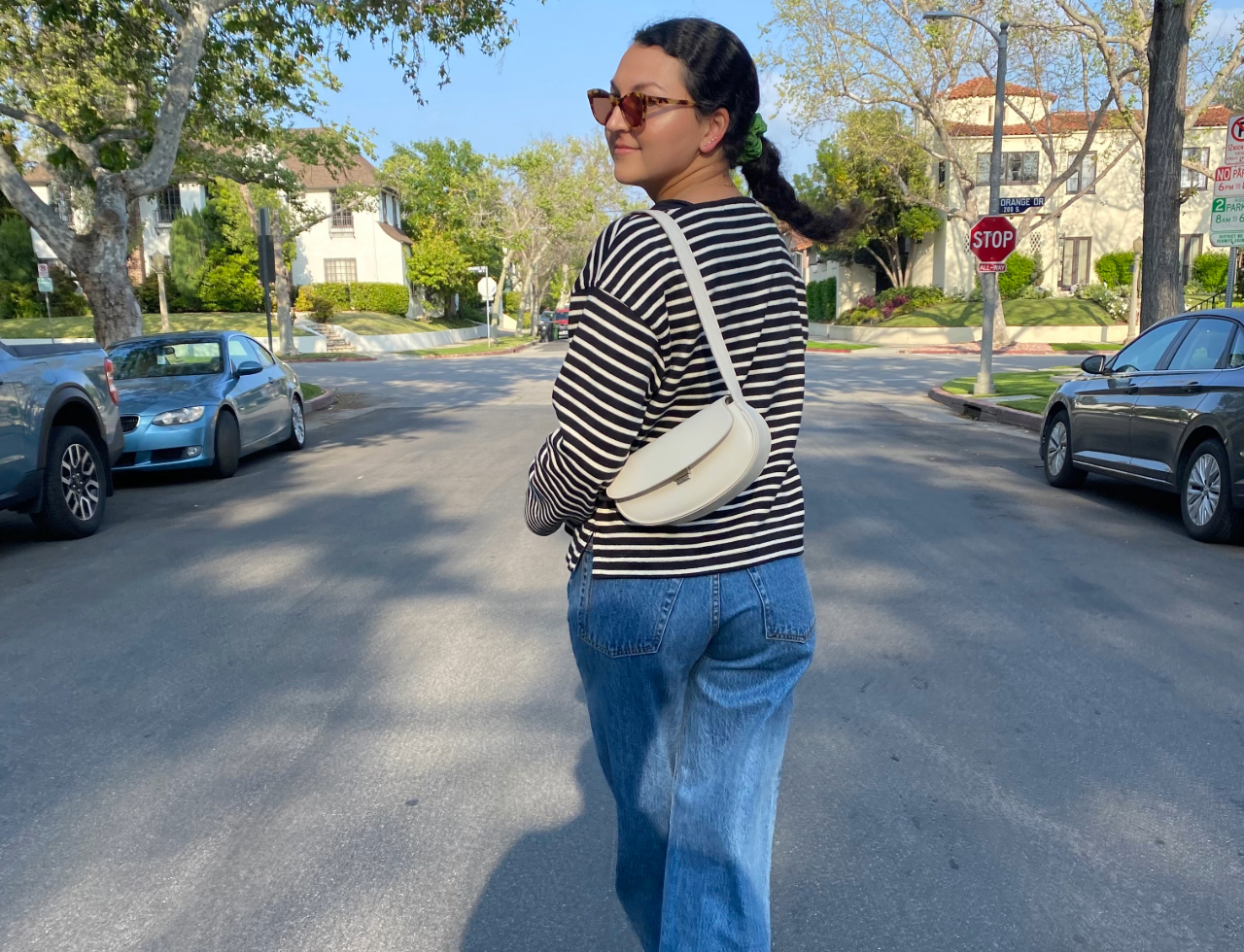 Woman in a striped T-shirt, jeans, with a cream crossbody bag.