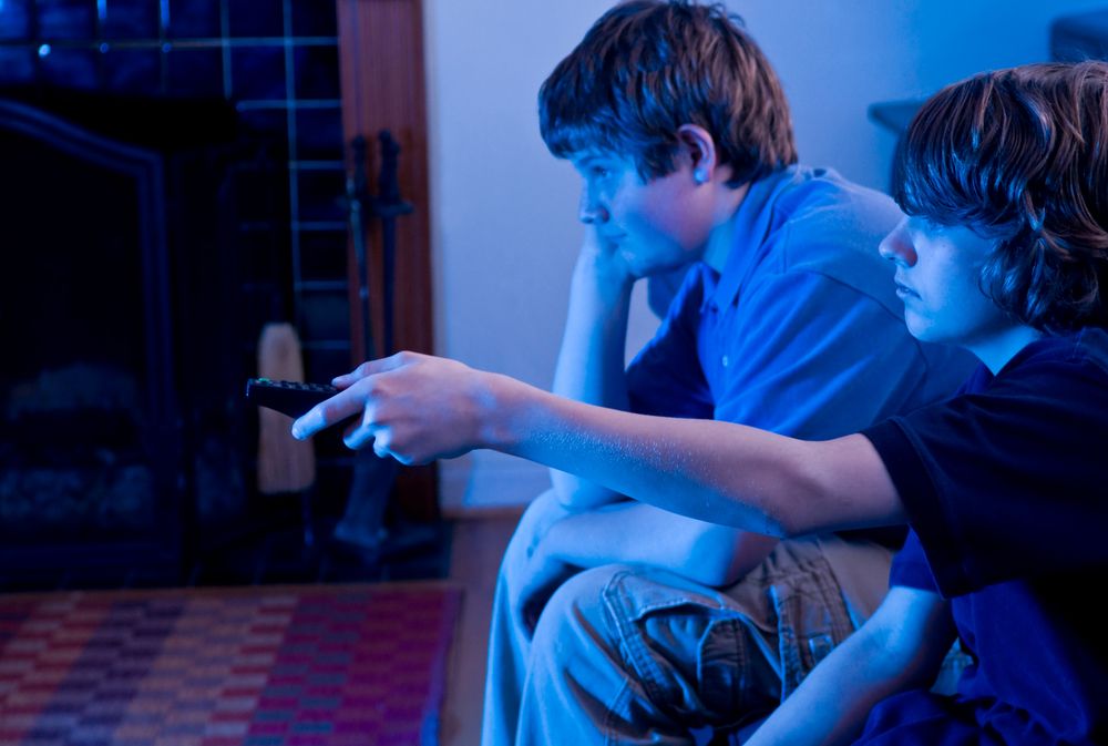 Two boys sit in a dark room watching television