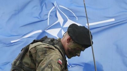 A Polish solider in front of a Nato flag