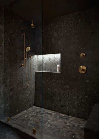 A dark bathroom with low lighting. This bathroom has been tile drenches with dark/black tiles.