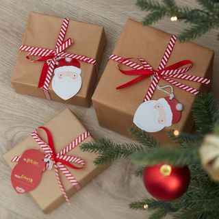 Christmas presents wrapped in brown wrapping paper with santa tags and red ribbons, with a few branches and baubles visible to show they are under a Christmas tree