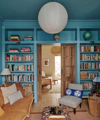 living room with blue color-drenched walls and ceiling, warm brown sofa, built-in book shelves and striped accent chair