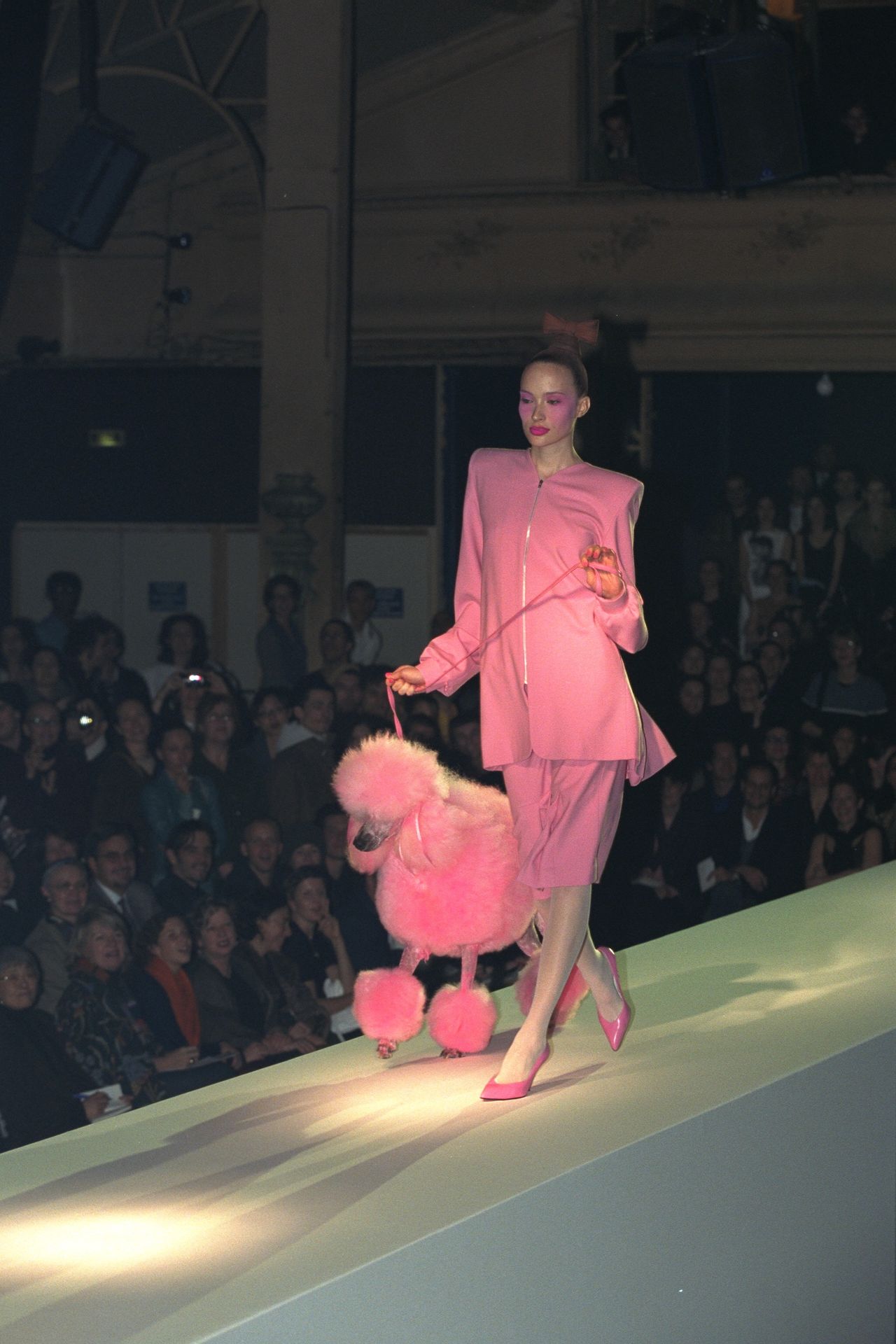 A model in a pink outfit walks a bright pink poodle down the catwalk during a fashion show.