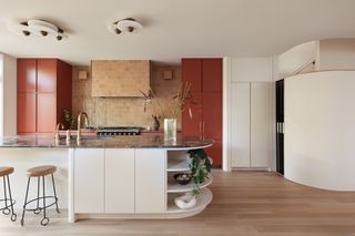 Red kitchen cupboard, white island with dark marble worktop and rounded edge