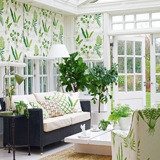 White conservatory with green leaf patterned blinds and armchair