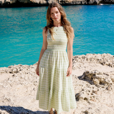 Model stood in front of a turquoise lake wearing a nobody's child light green gingham midi dress 