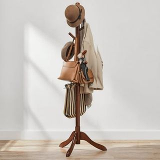 a brown wooden coat rack, free standing, with coats, bags, and a hat hanging from it. 