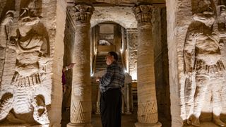 a tourist standing in an old doorway. on either side are big stone carvings showing large figures