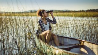 lady in a boat on the water looking out with binoculars