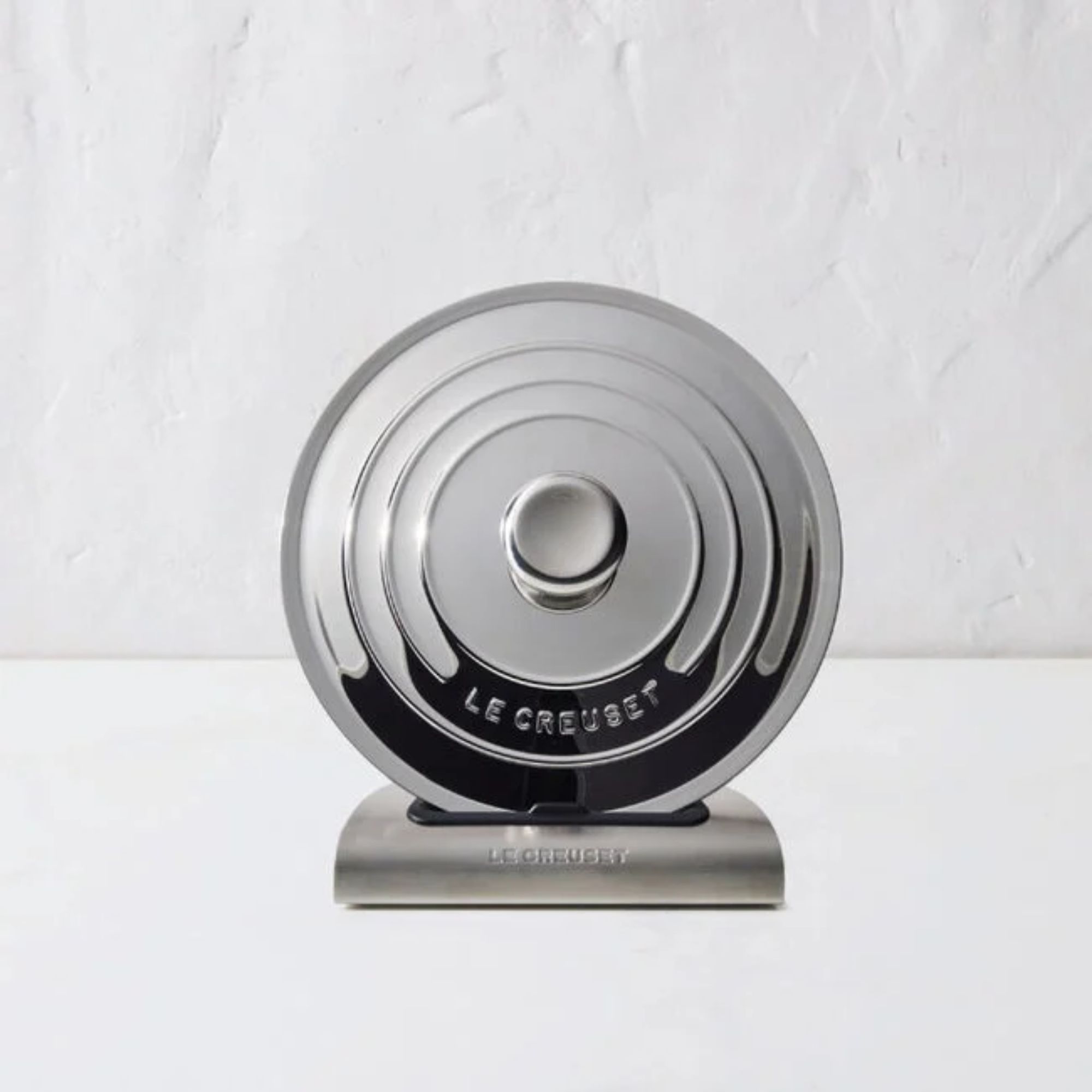 A stainless steel pan lid being held upright by a stainless steel stand.