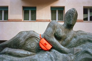 Stone figure sculpture wearing bold orange handbag