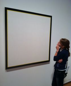 Young woman looks at blank framed image on wall.