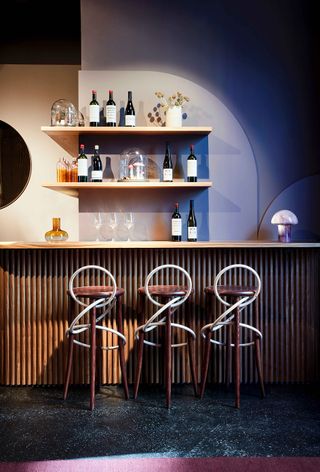 Lindley Lindenberg bar with wooden wall shelves and bar stools with intertwined circles of steel for backrest
