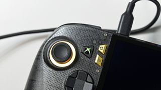 Close-up of the ROG Ally X20 left grip with dbrand skin, illuminated joystick ring, and glowing green Xbox guide button