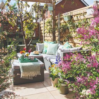 A blooming patio with a wooden fence and a chaise outdoor sofa with a matching ottoman