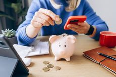 a woman sitting at her desk depositing coins into a piggy bank 